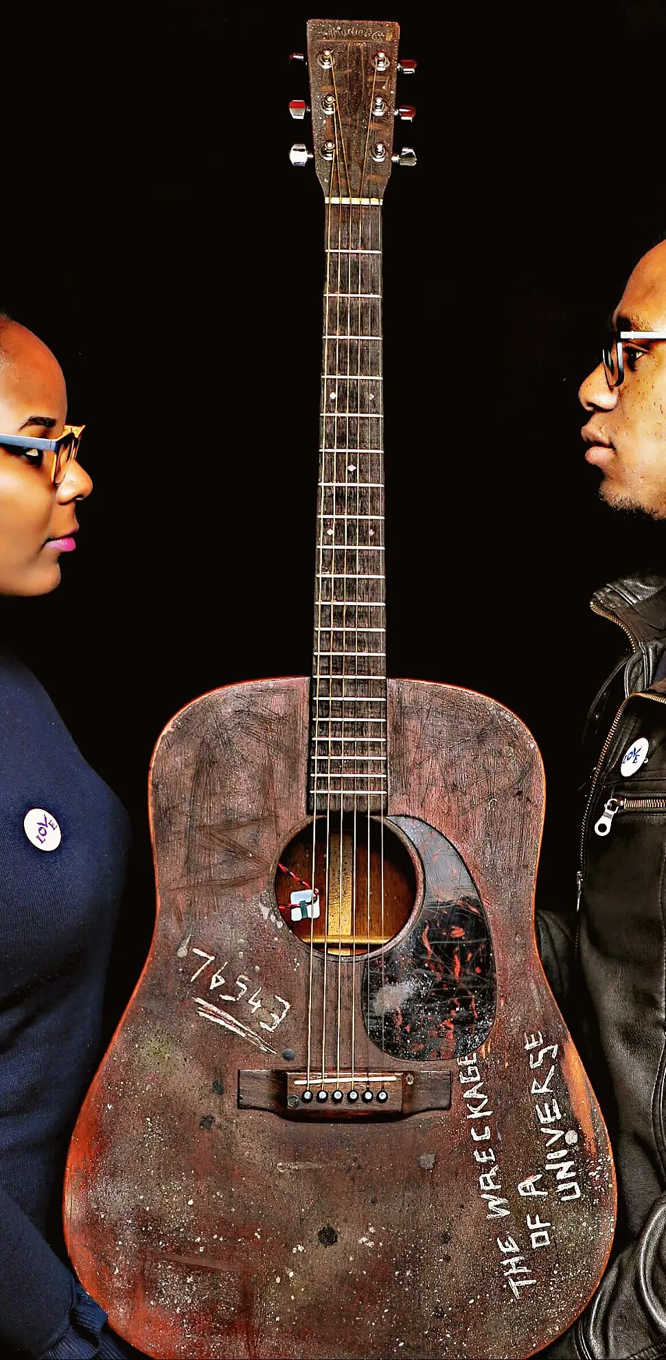 Sarah Knew: two band members face each other across a battered acoustic guitar against a black backdrop
